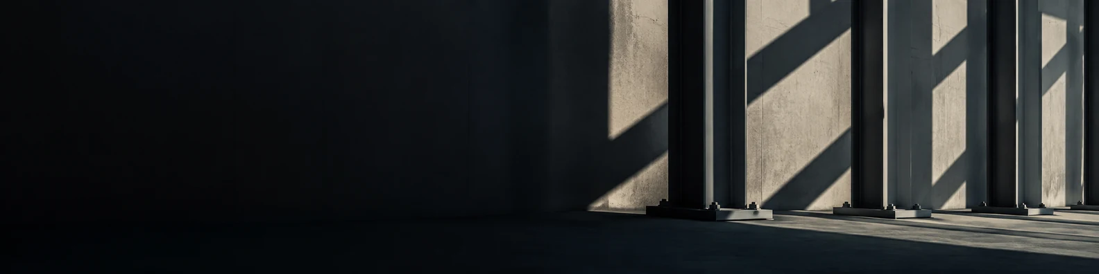 Structural steel columns casting crisp diagonal shadows with a deep dark open foreground on the left