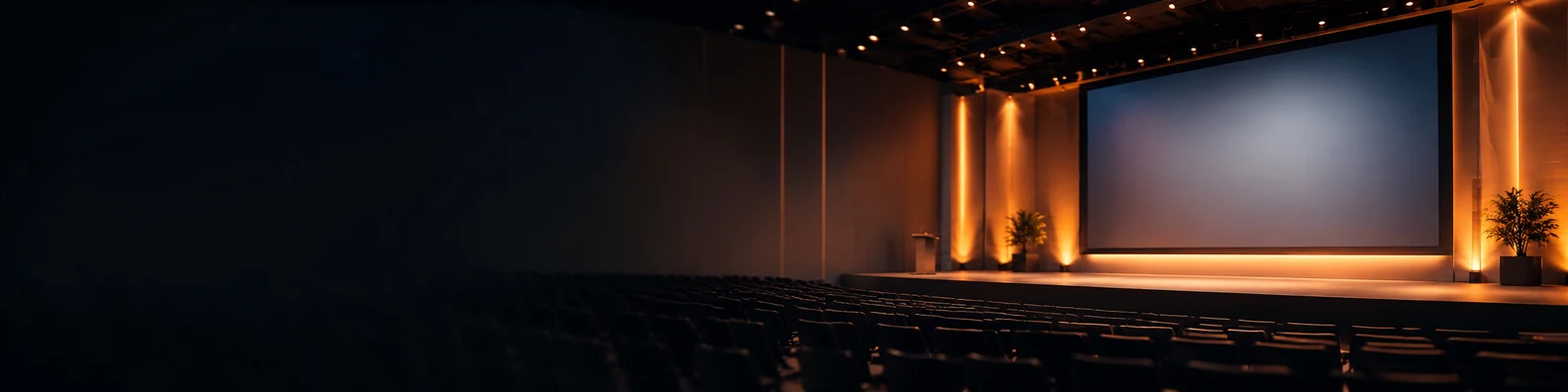 Softly blurred corporate auditorium with warm stage lights large blank screen and dark simple left seating area